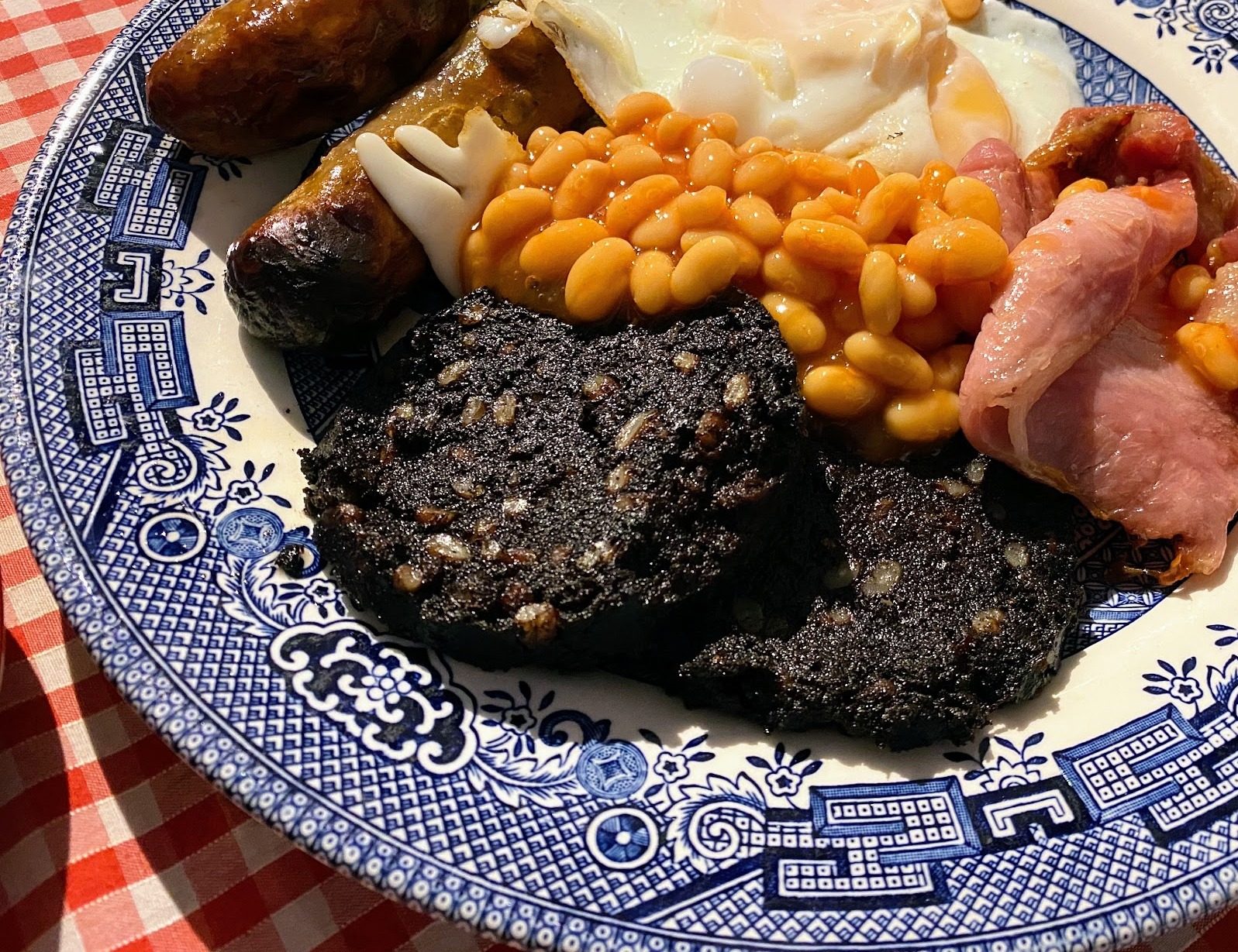 A cooked breakfast with black pudding, beans and bacon on a blue-and-white plate